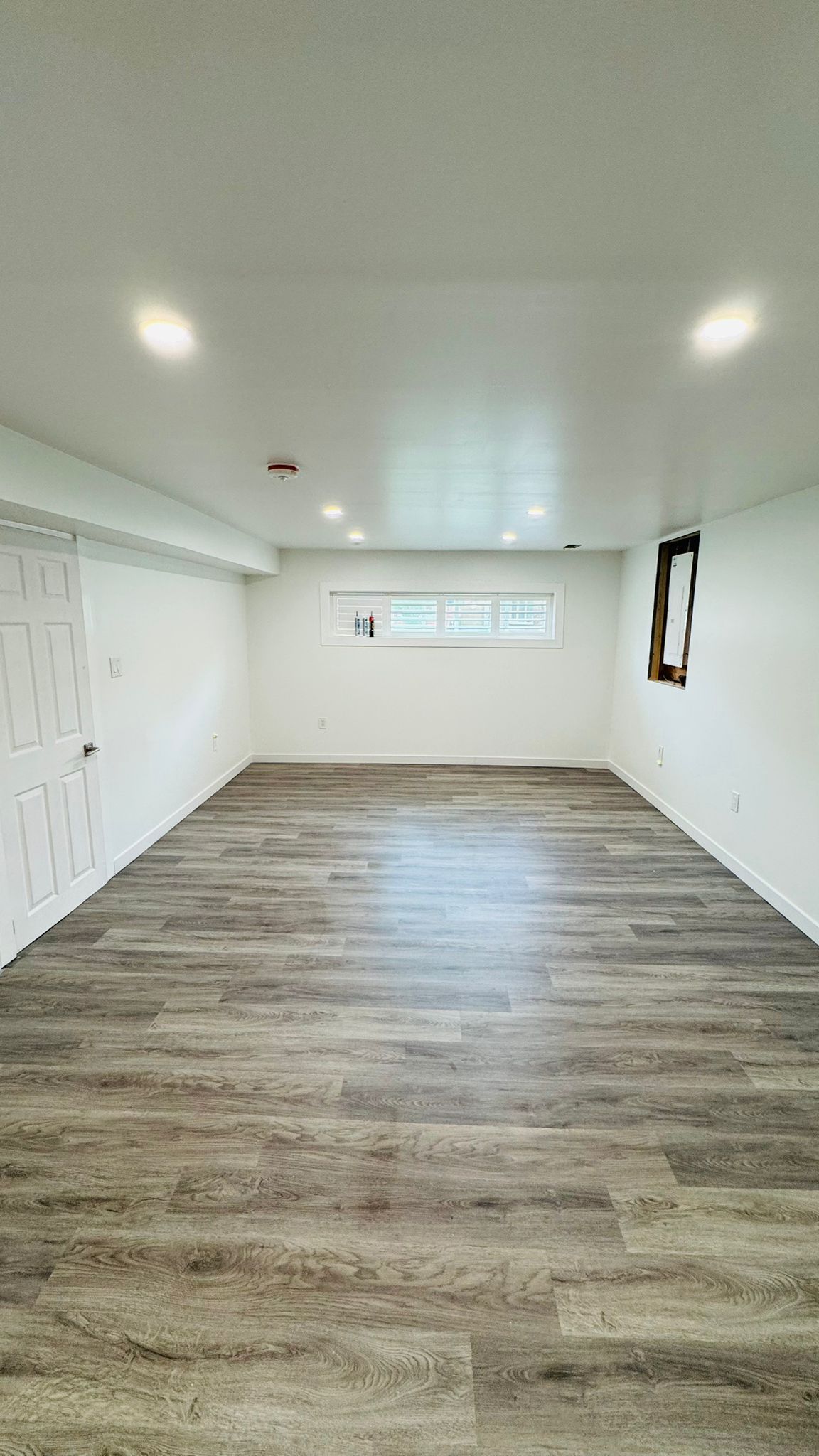 Bright finished basement room with pot lights and egress window shutters