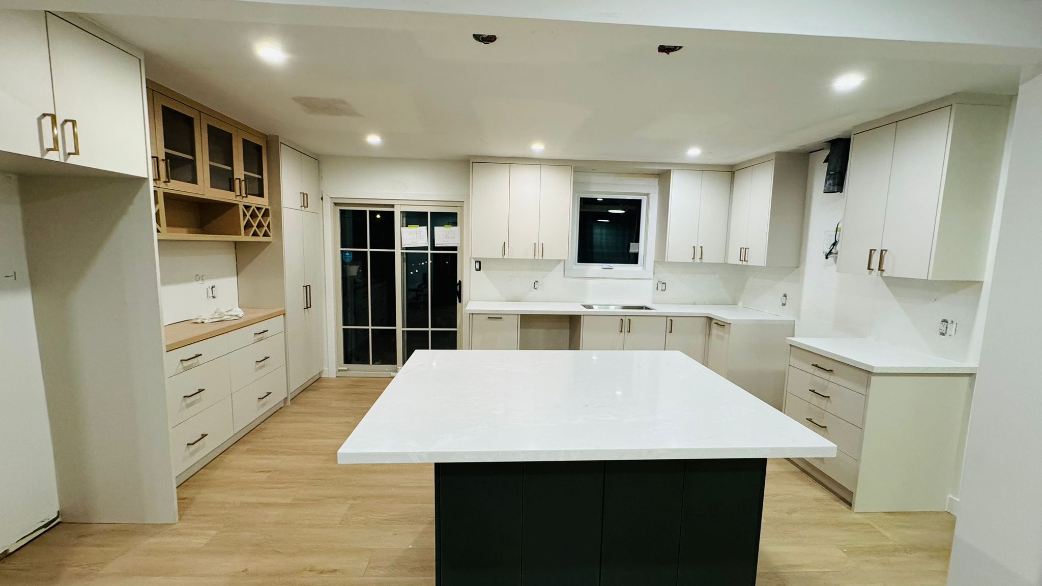 Finished kitchen with a dark green island, white cabinetry and quartz counters
