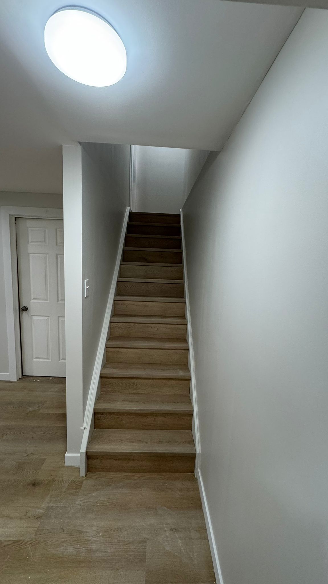 Basement staircase with oak treads leading up to a flush ceiling light